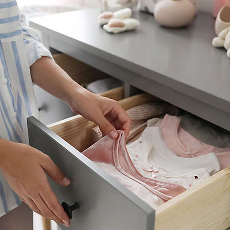 person placing folded baby clothes in drawer